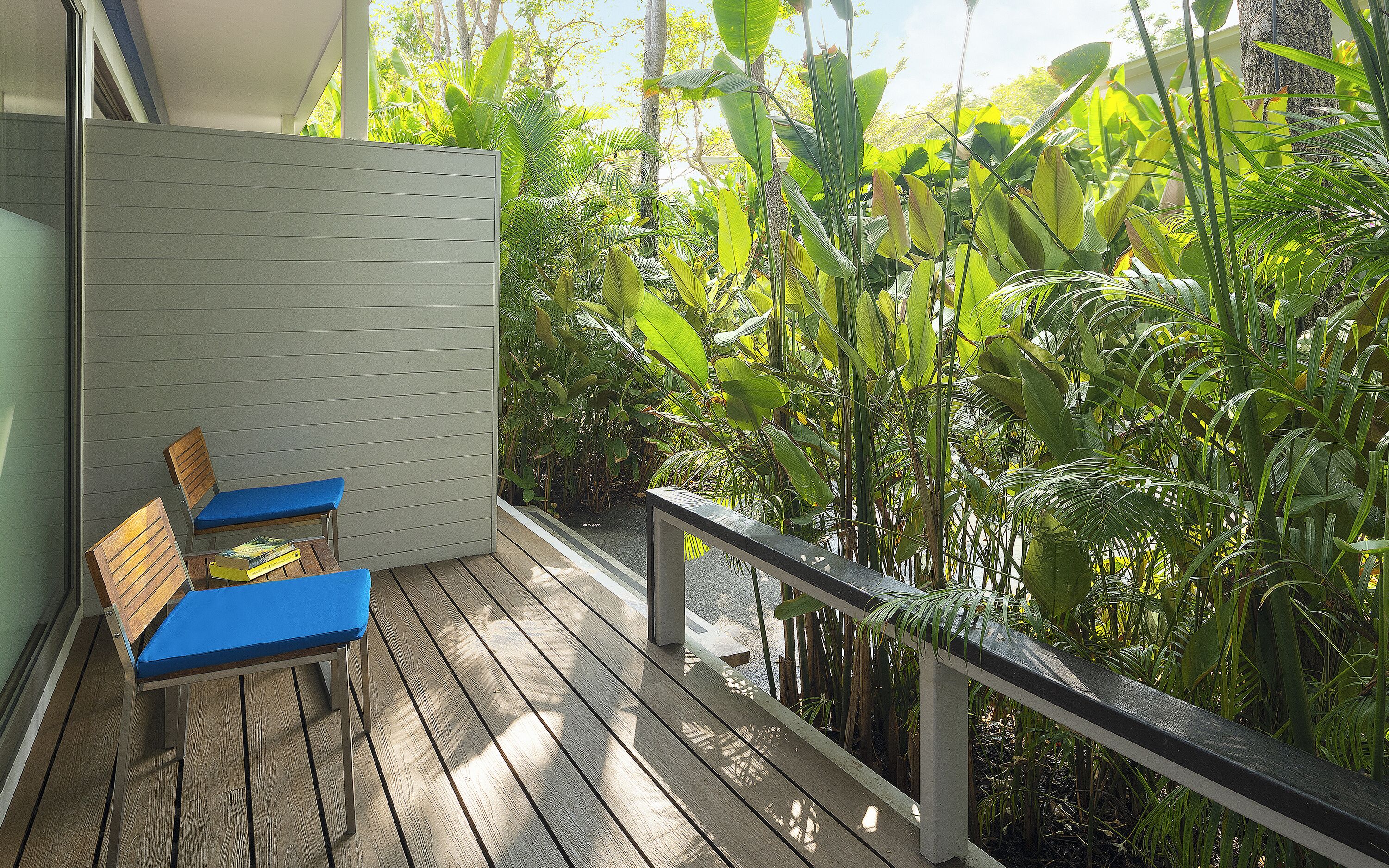 A wooden deck with two blue chairs, surrounded by lush tropical plants.