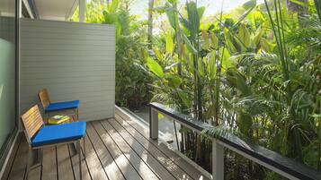 A wooden deck with two blue chairs, surrounded by lush tropical plants.