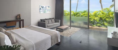 A modern hotel room with a large bed, a sofa, a coffee table, and a view of the ocean through floor-to-ceiling windows.