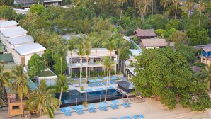 An aerial view of a resort with a swimming pool, beach chairs, and palm trees.