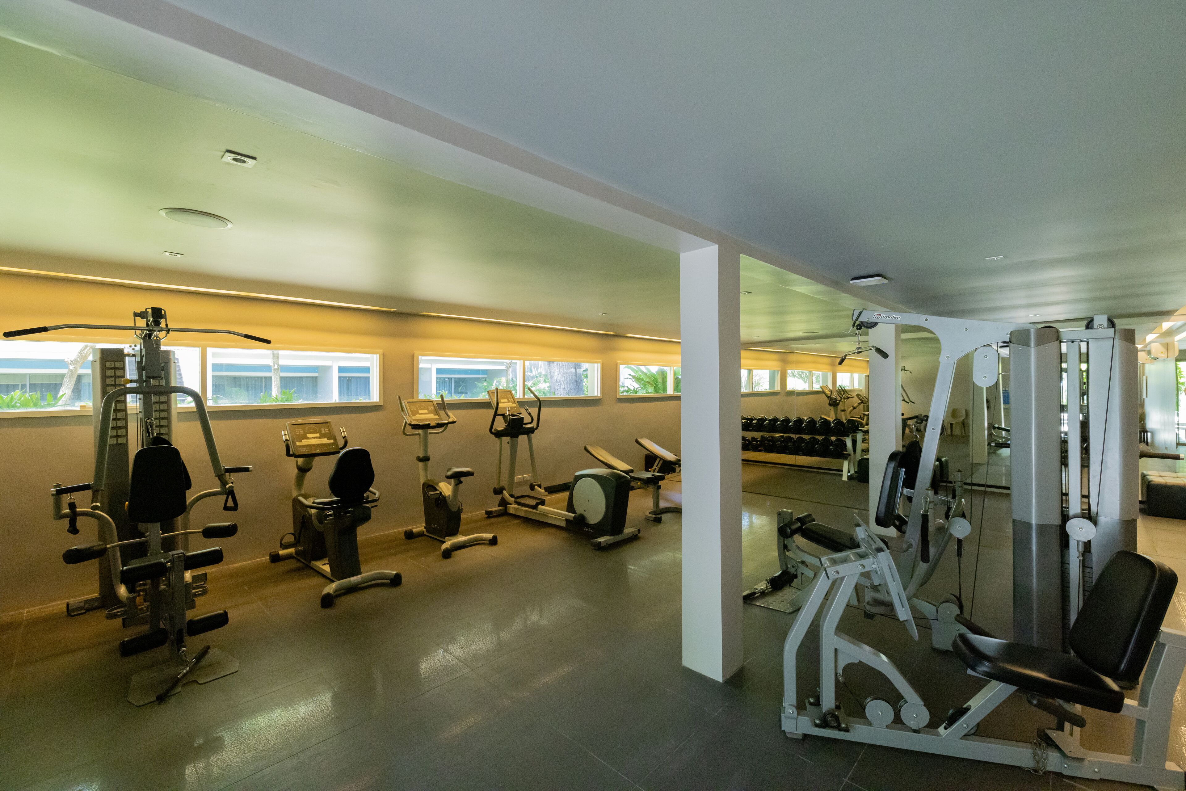 Un gimnasio con diversas máquinas de ejercicio, una banca de pesas y mancuernas.