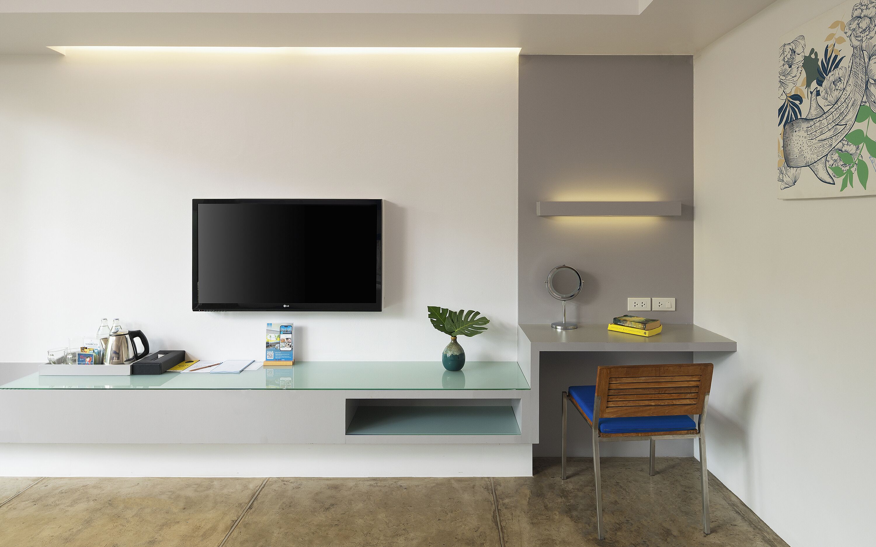 A modern living room with a flat-screen TV mounted on the wall, a glass coffee table, a wooden chair, and a small plant.