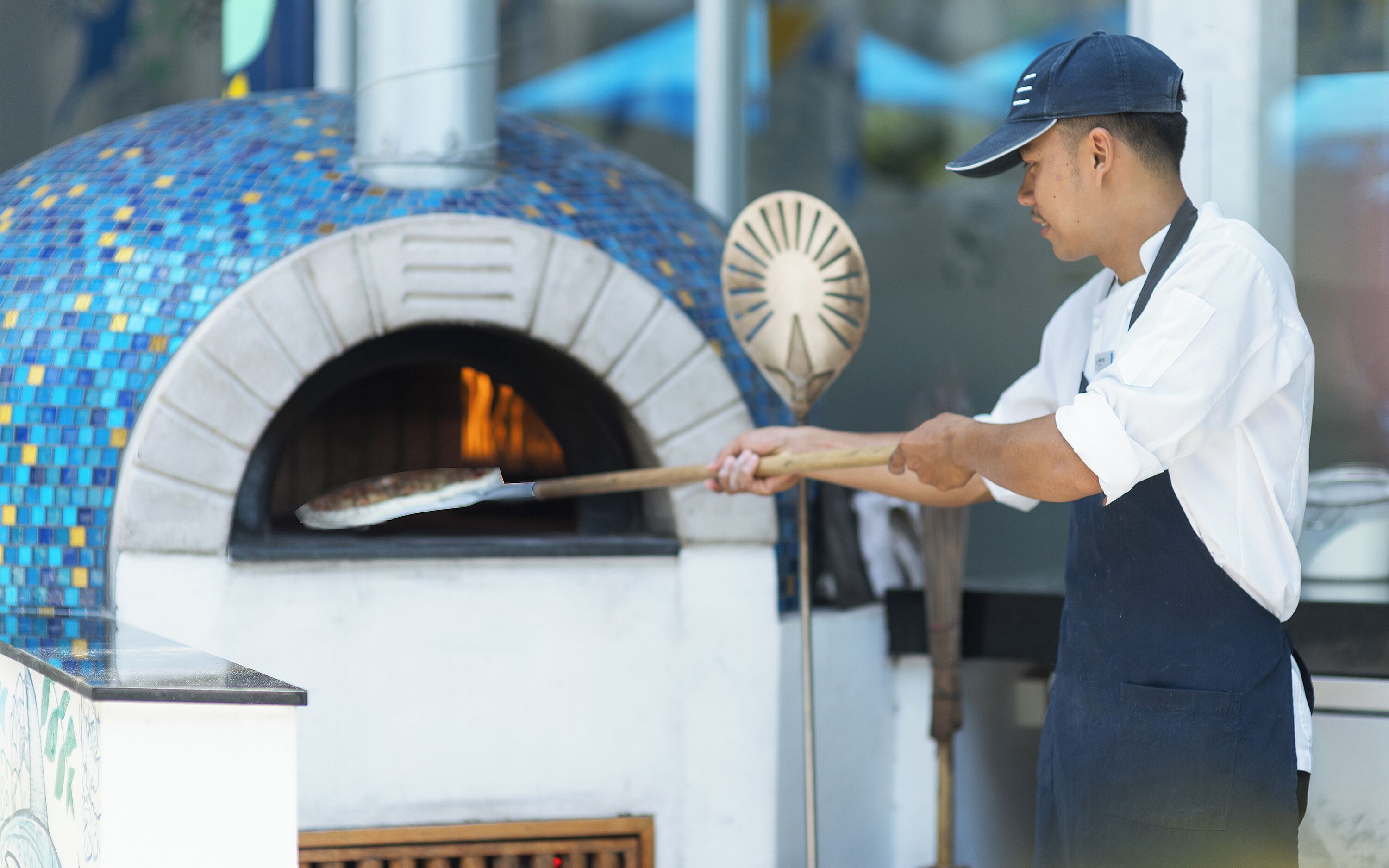 Iemand gebruikt een lange tang om een pizza uit een bakstenen oven te halen.