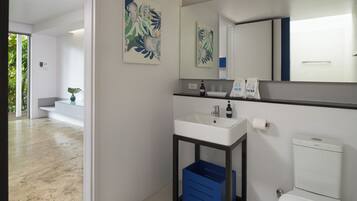 A modern bathroom with a white sink, a mirror, and a toilet. There are two towels hanging on the wall, and a blue storage bin under the sink.