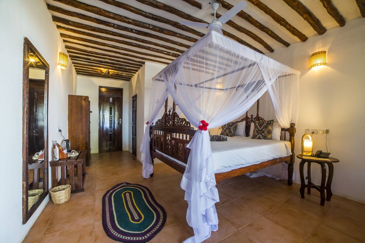 A bedroom with a four-poster bed, a bedside lamp, and a woven rug.