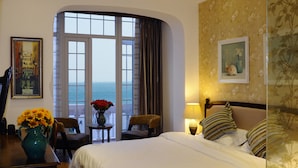 A hotel room with a large window, a bed, a chair, a table with a vase of flowers, and a lamp. - Qingdao Villa Inn Seaside (Qingdao)