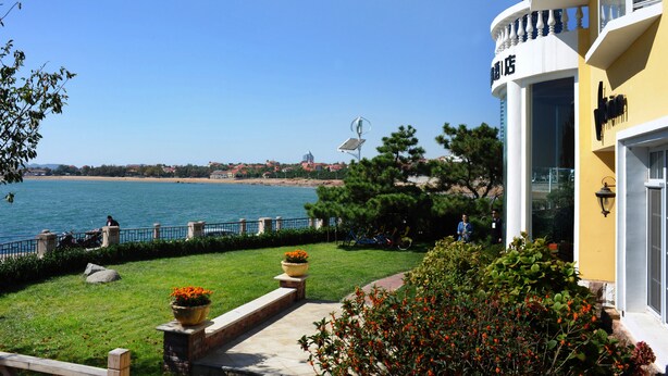 A waterfront hotel with a view of the sea and a distant cityscape. - Qingdao Villa Inn Seaside (Qingdao)
