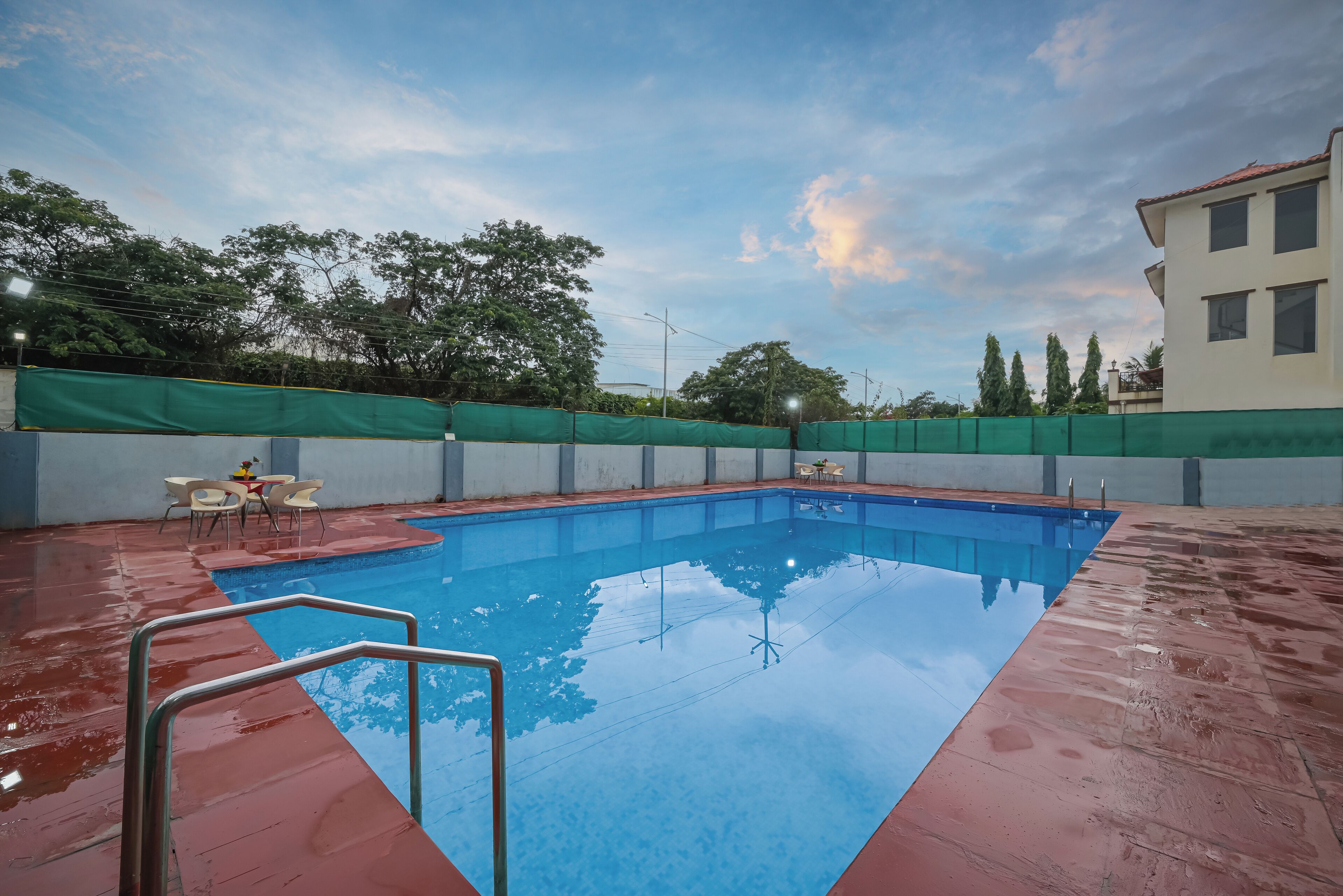 Une piscine rectangulaire avec un escalier en métal au premier plan, entourée d’une terrasse rouge.