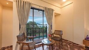 A balcony with two wooden chairs, a small table with a book and vase, and a view of the cityscape. - Hotel Aristro (Mawal)