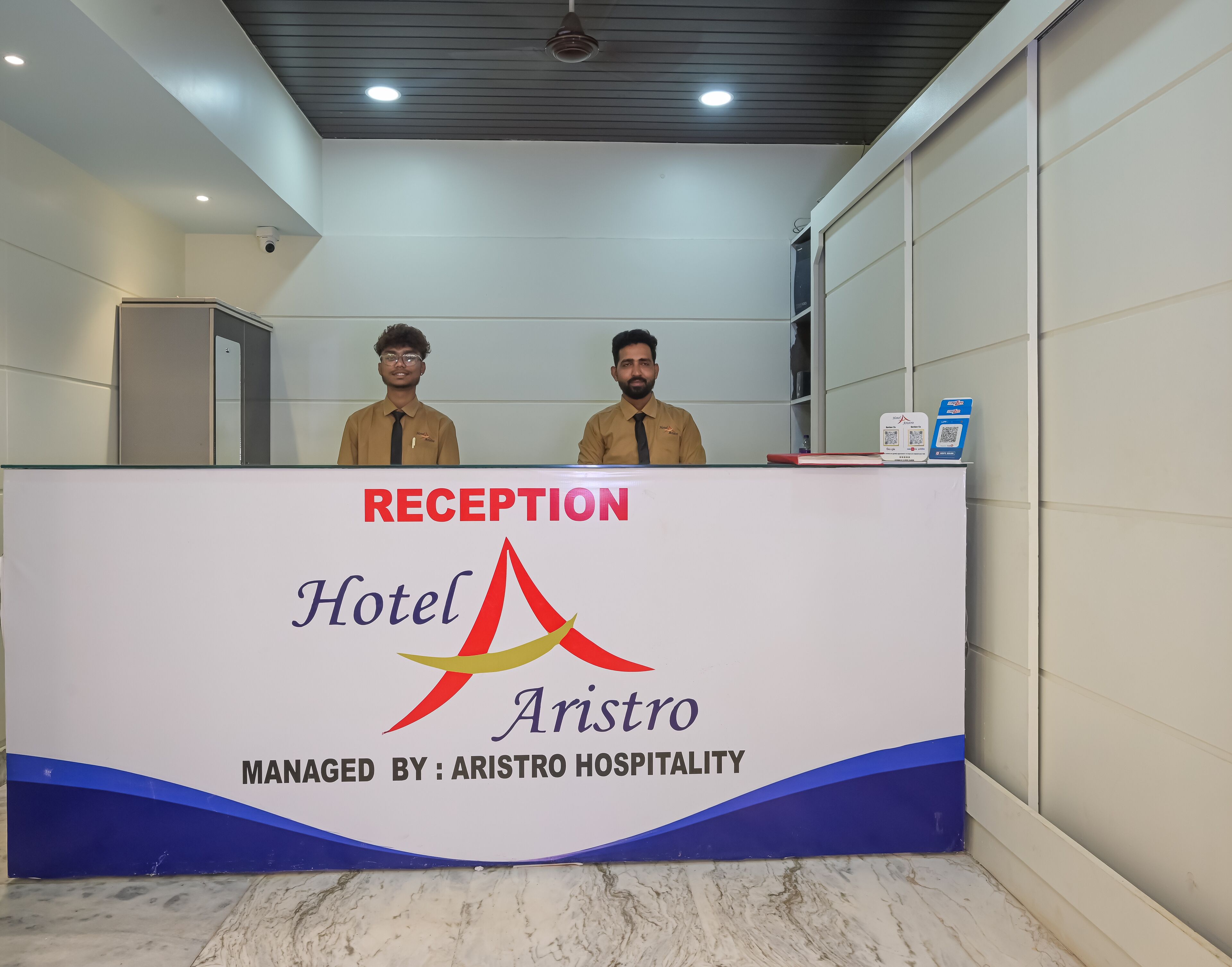 Eine Rezeption im Hotel Aristro, mit einem Schild, das bestätigt, dass es von Aristro Hospitality verwaltet wird.