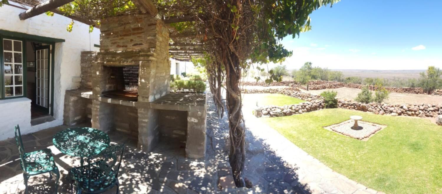 Cocina exterior de piedra con chimenea, rodeada por un césped cuidado y muros de piedra.