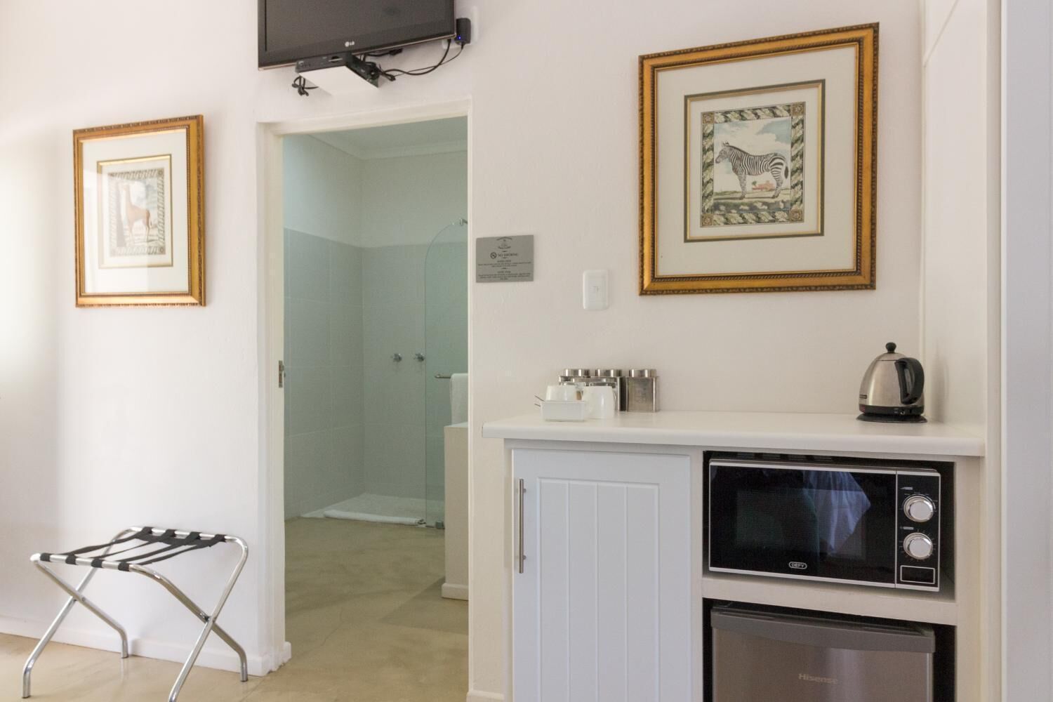 Une cuisine compacte équipée d’un four à micro-ondes, d’une bouilloire et de placards. Il y a également un espace douche avec des portes en verre et un porte-serviettes.