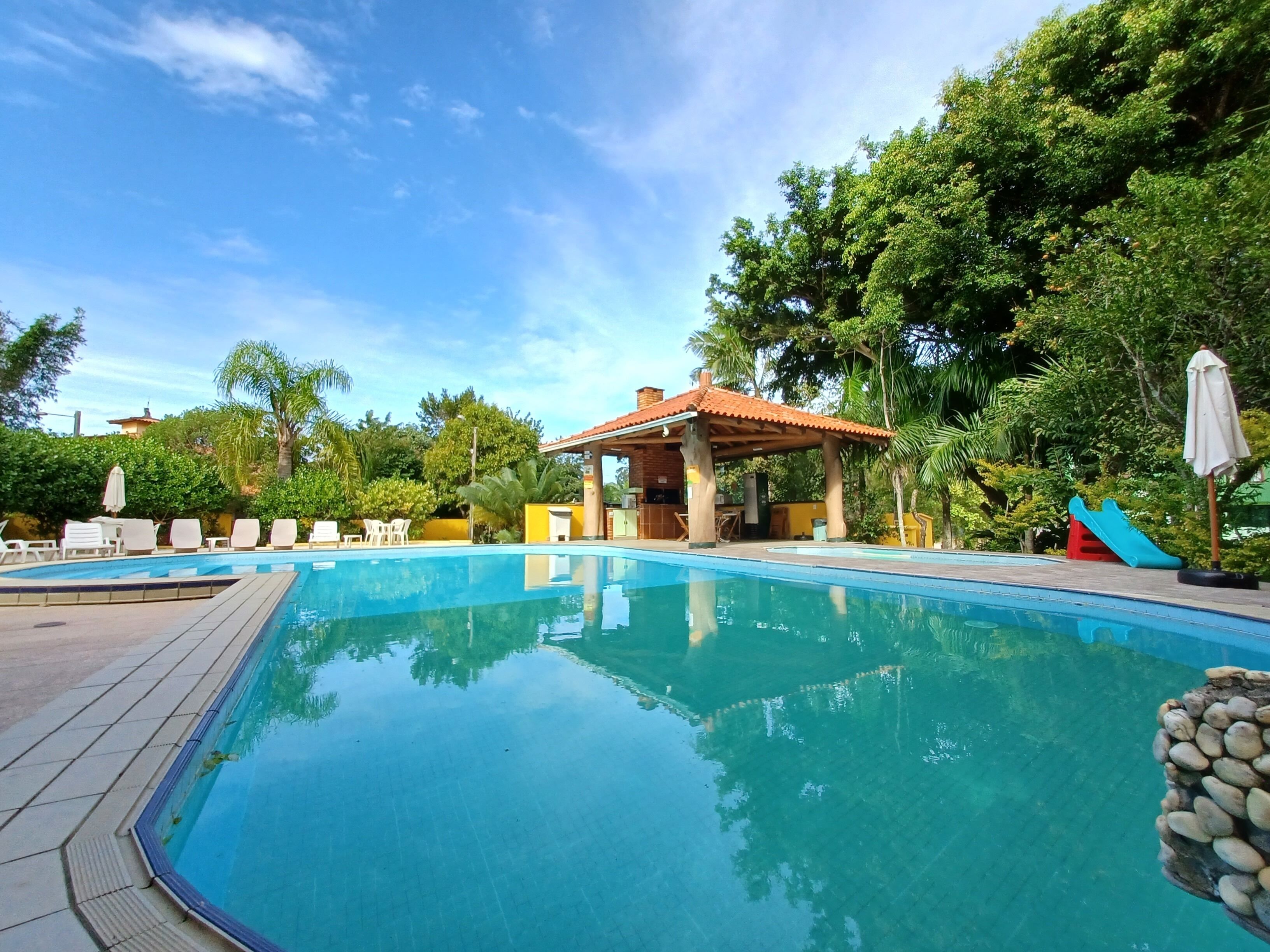 Una piscina azul cristalina con sillones de descanso y una zona sombreada.