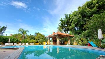 Una piscina azul cristalina con sillones de descanso y una zona sombreada.