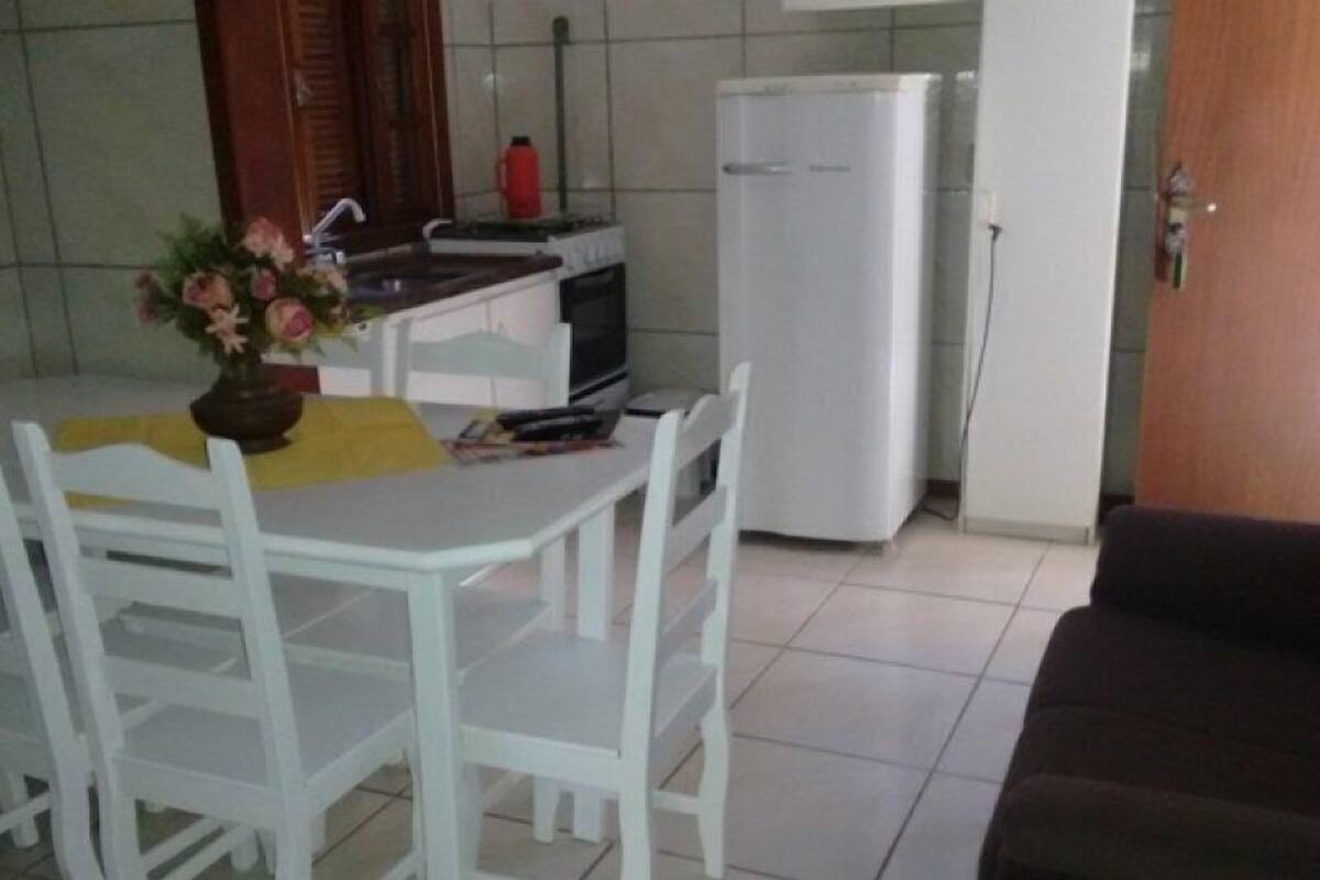 Eine kleine Küche mit weißem Tisch, Stühlen, einem Kühlschrank und einem Spülbecken.