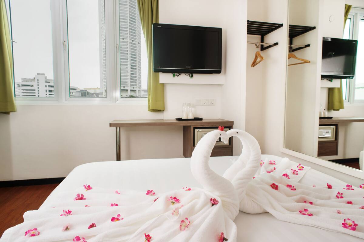 Una habitación de hotel con una cama, televisión de pantalla plana, escritorio y espejo.