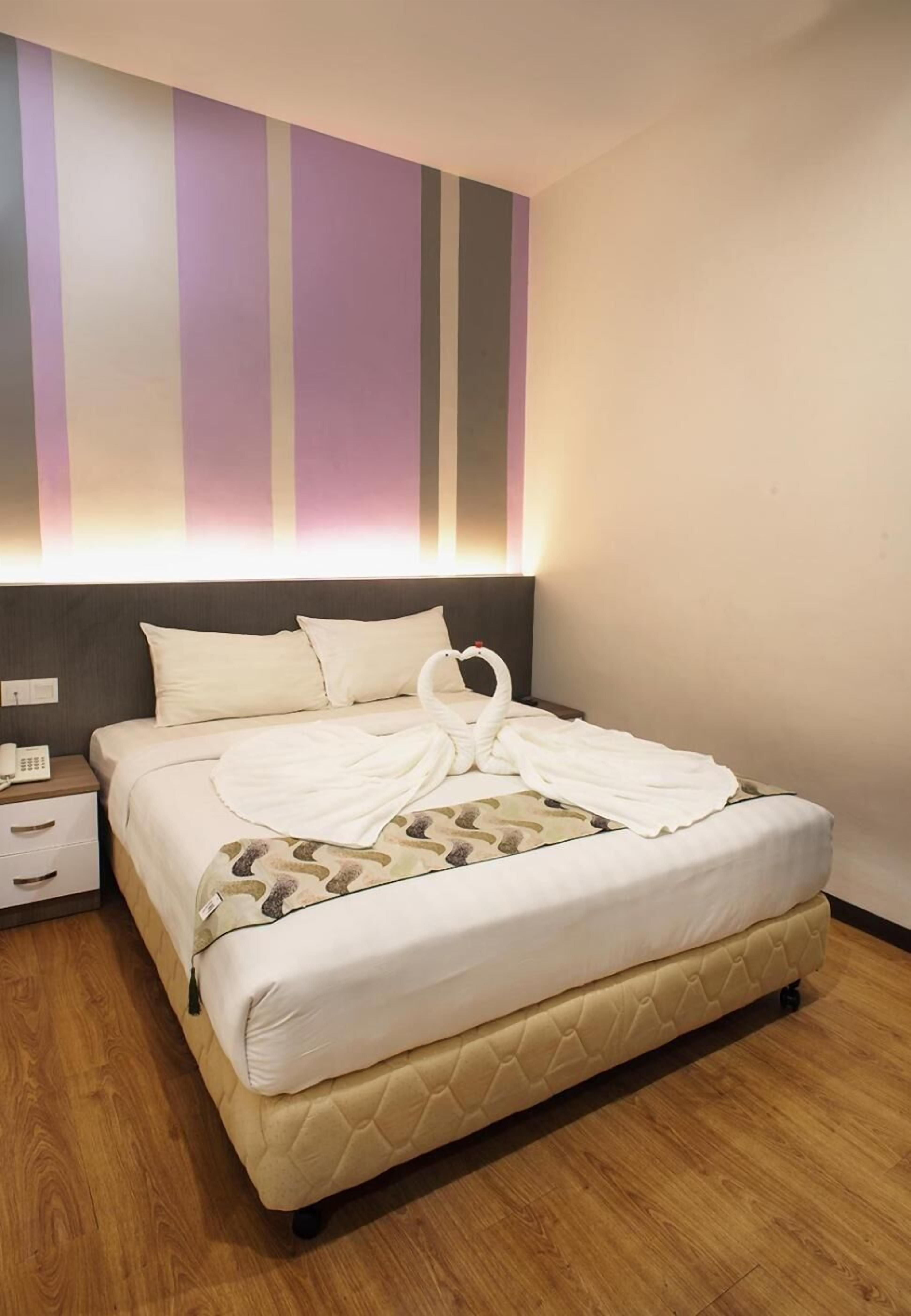 Una habitación de hotel con una cama, una mesita de noche, un teléfono y una pared a rayas verticales.