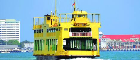 A yellow ferry named PULAU RIMAU PENANG with a clear view of the water and a building with a red roof in the background.