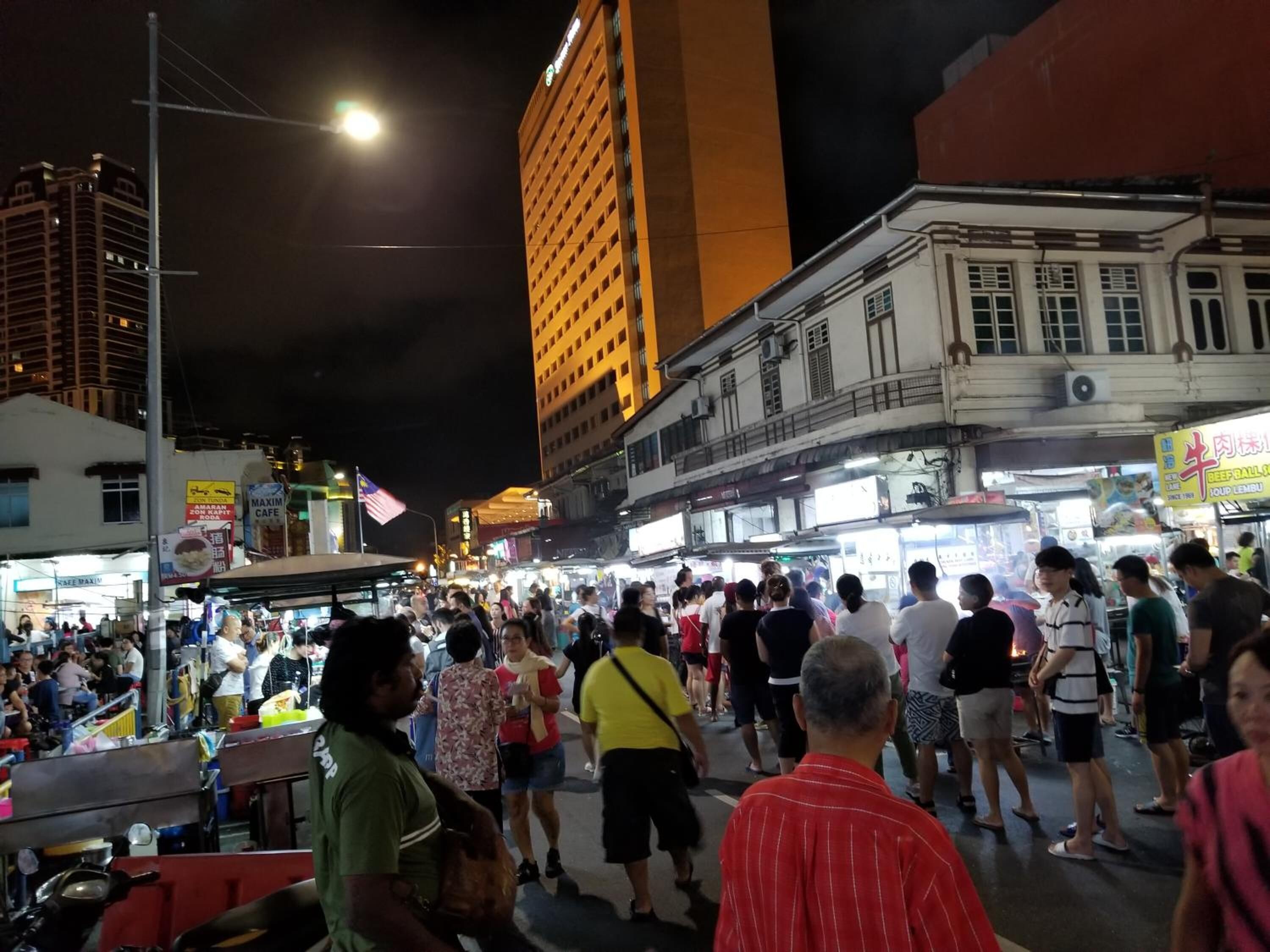 A crowded street at night with tall buildings and illuminated signs.