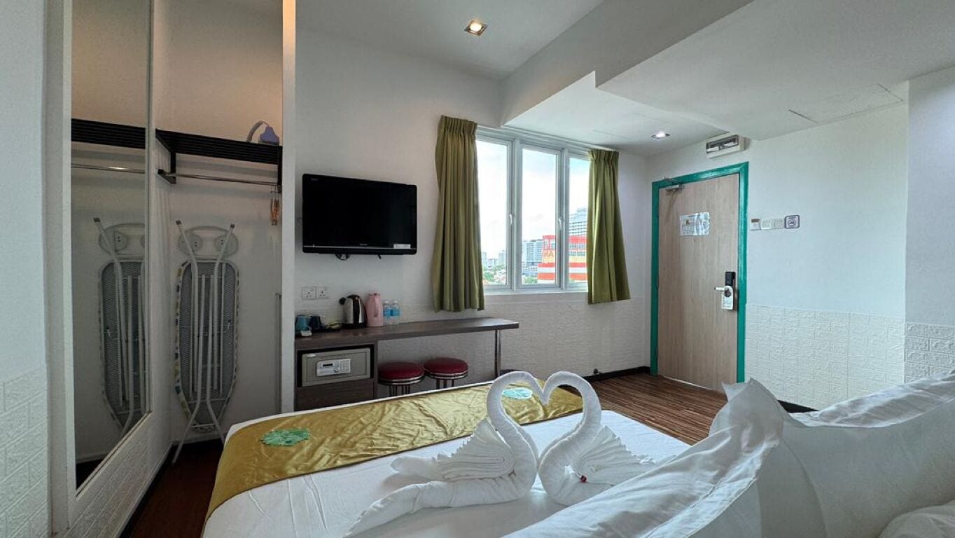 Une chambre d’hôtel avec un lit agrémenté d’une décoration en forme de cygne, un téléviseur fixé au mur, un bureau avec une chaise et une fenêtre avec des rideaux.