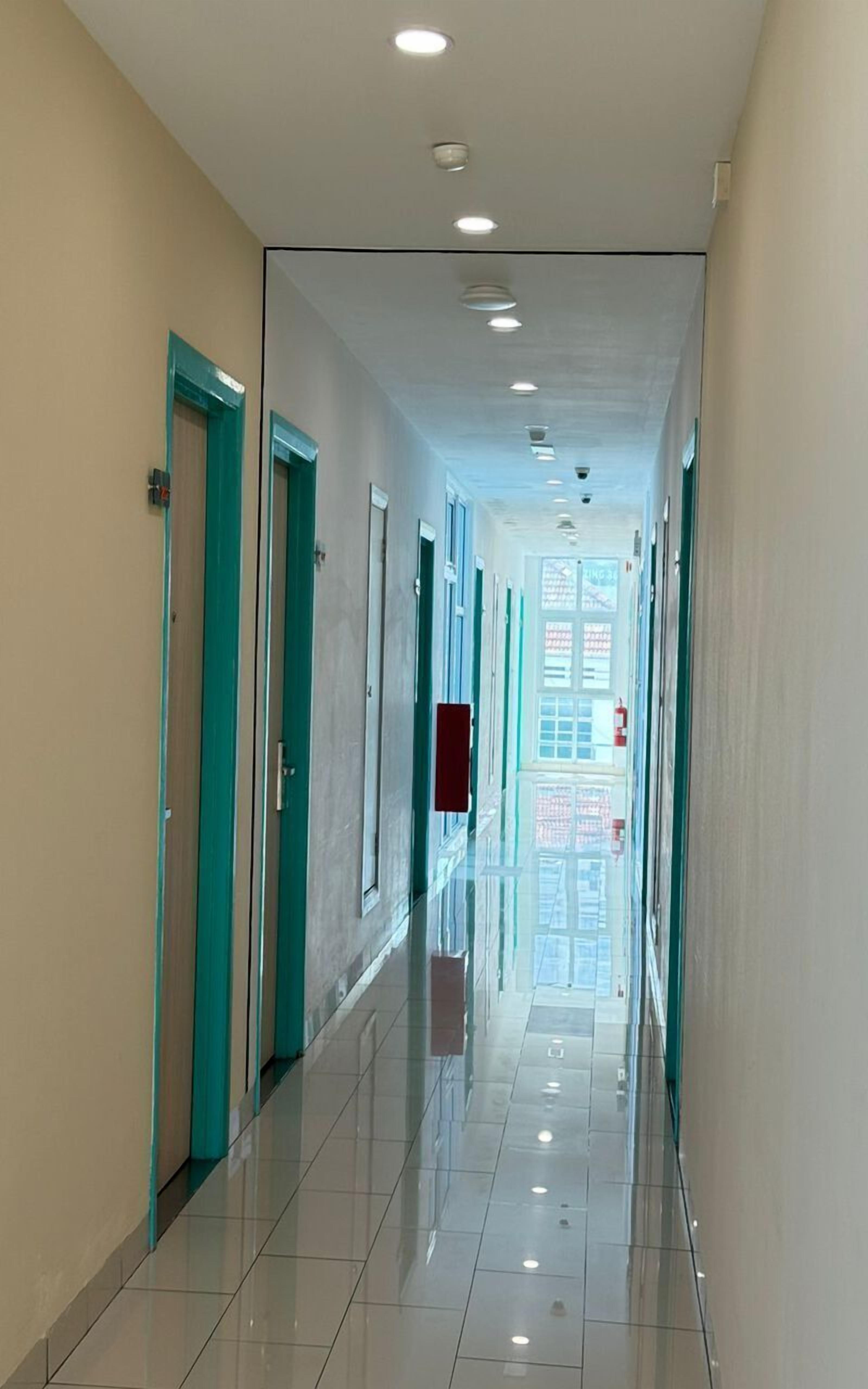 A long, well-lit corridor with teal-framed doors, a clean tiled floor, and a view of a building outside.