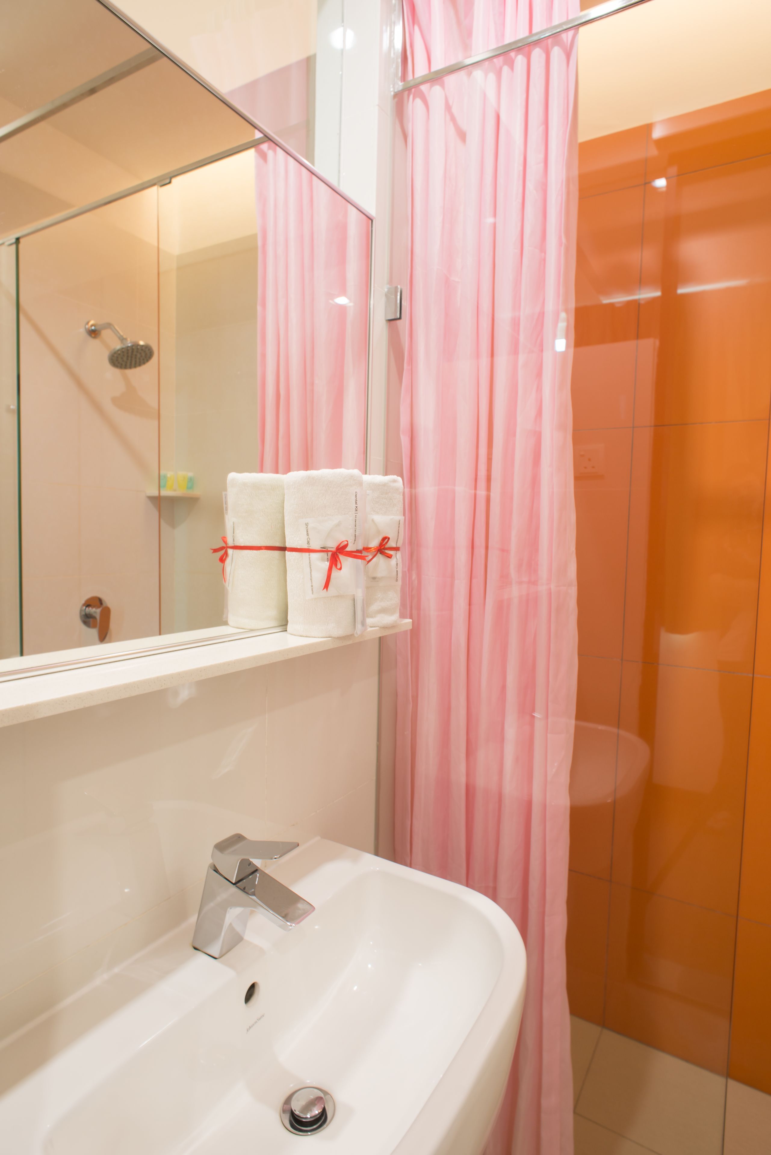 A bathroom with a white sink, a mirror, and a shower with a pink curtain. There are two towels on the sink.