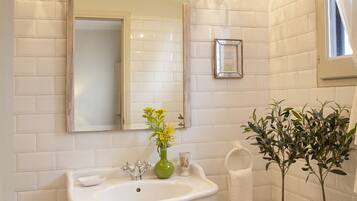 Une salle de bain avec un lavabo sur colonne, un miroir, un lustre et des plantes en pot.