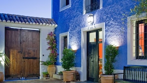 Een blauw gebouw met een houten deur, bloempotten en een bank.