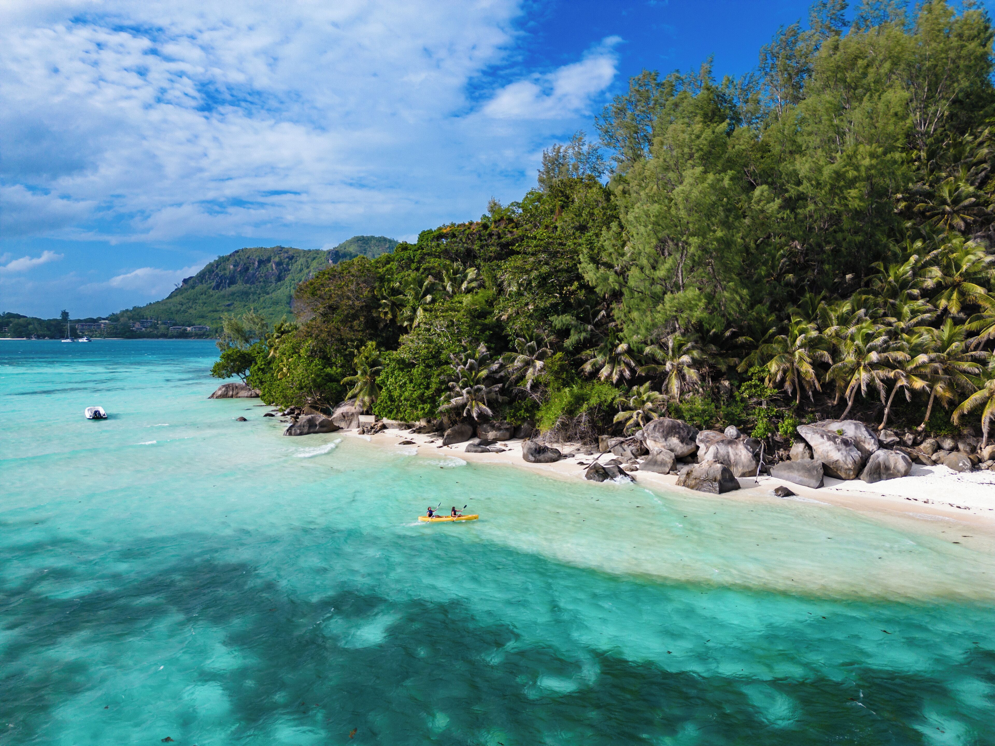 A beach with clear turquoise water, rocky shoreline, and dense tropical vegetation.