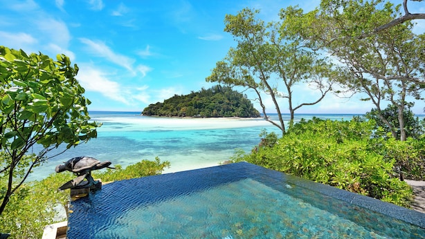 A clear view of a tropical beach with a tree-lined infinity pool overlooking the ocean. - Enchanted Island Resort (Round Island)