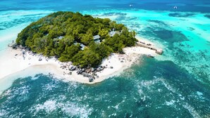 An aerial view of a tropical island with a beach, clear turquoise waters, and a small dock. - Enchanted Island Resort (Round Island)