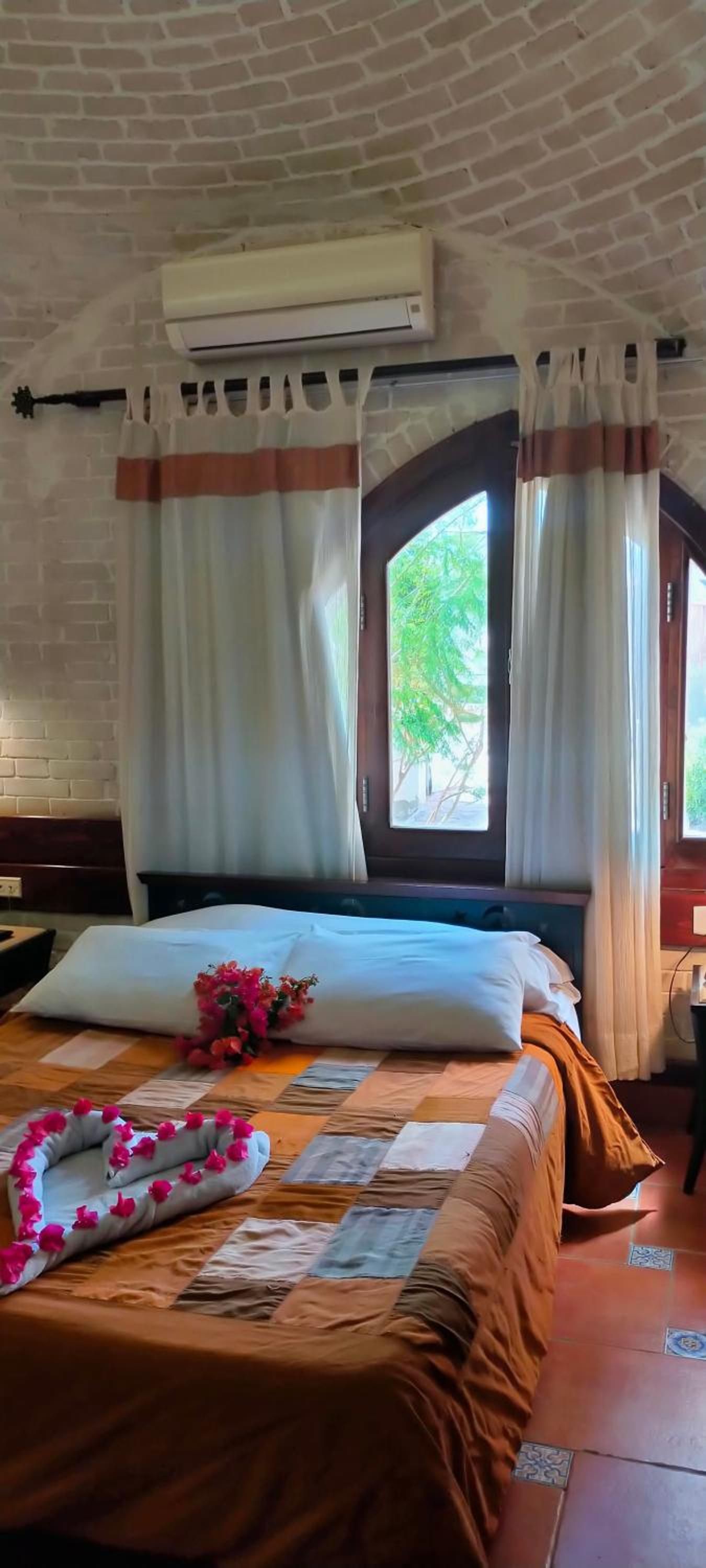 A hotel room with a bed, a window with curtains, and an air conditioning unit.