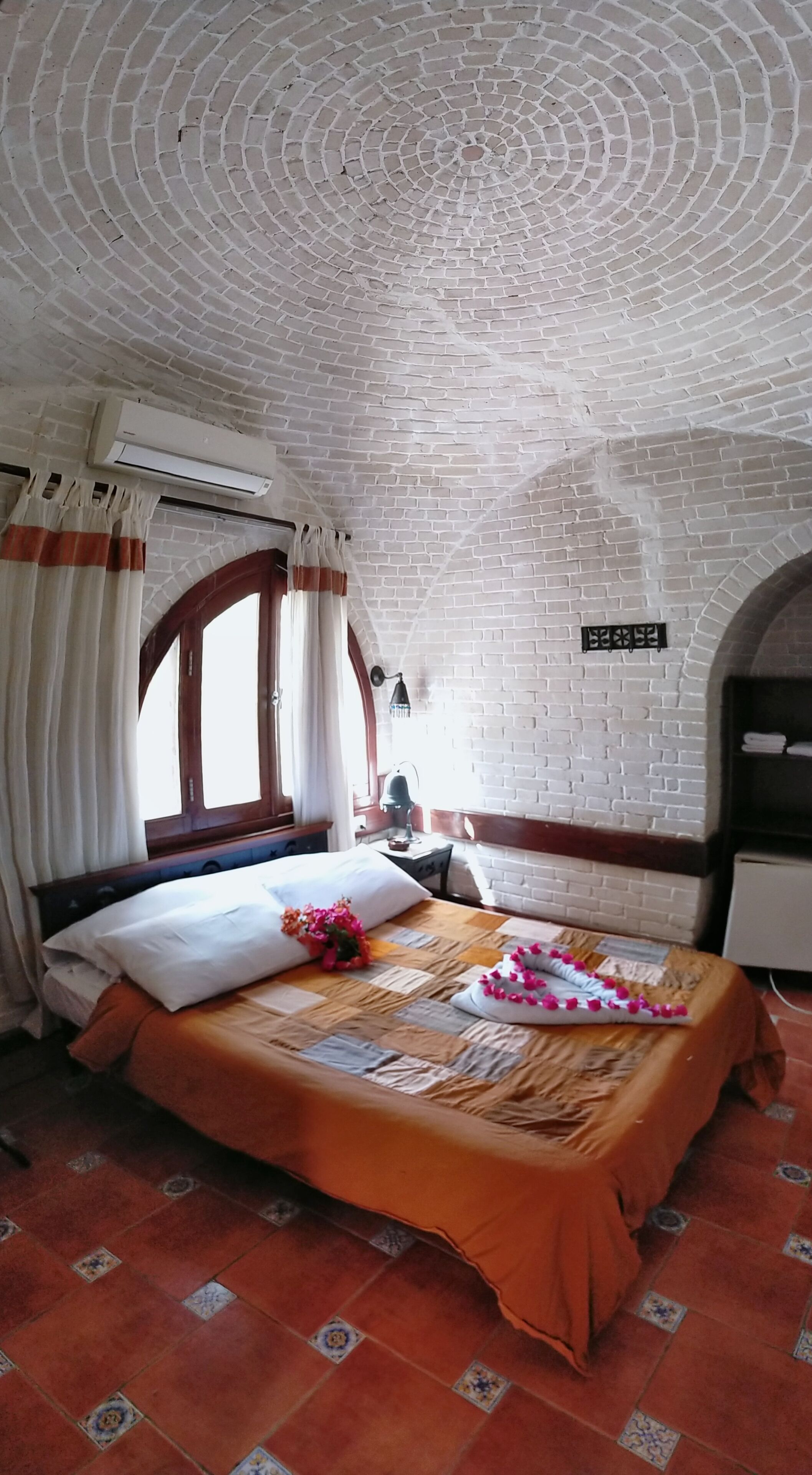 Una habitación con techo de ladrillo, una cama con colcha a cuadros, una ventana con cortinas y un aire acondicionado instalado en la pared.