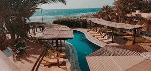 Un área de piscina en un resort, con una piscina en forma curva, sillas de descanso y sombrillas.
