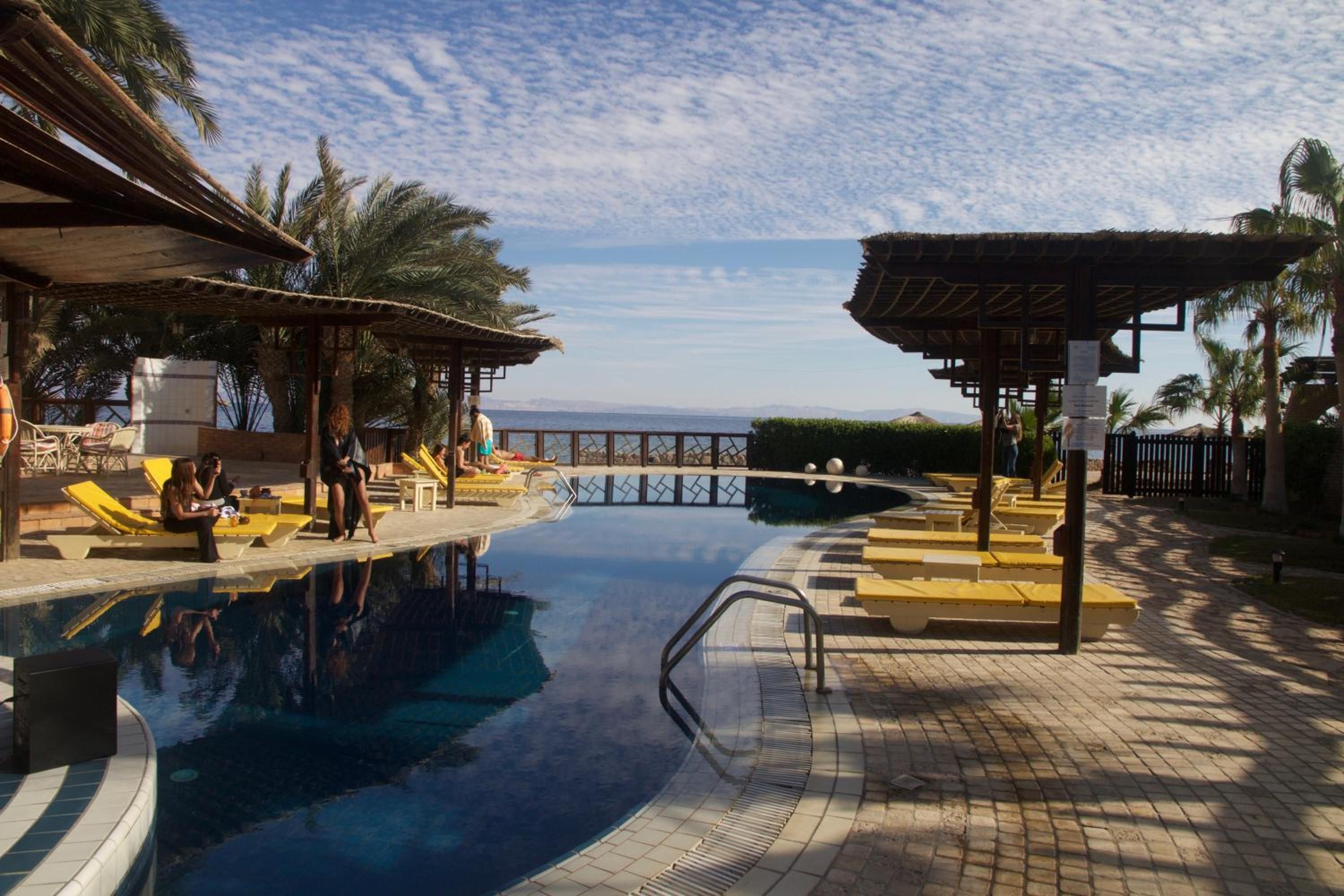 Un espace piscine comprenant des chaises longues, une piscine et une vue sur la mer.