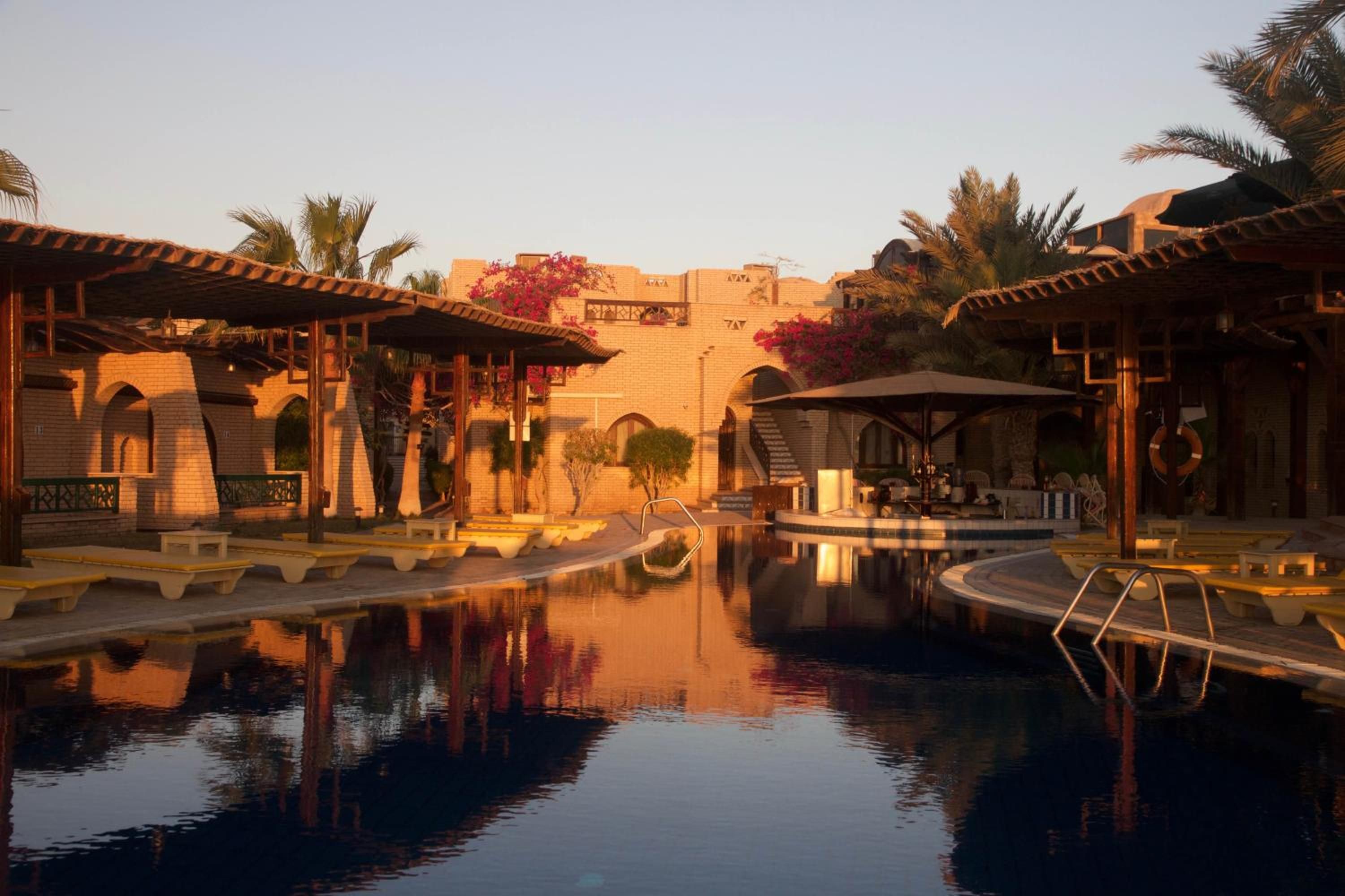 A pool area with a clear view of the pool, lounge chairs, and a building with a traditional architectural style.