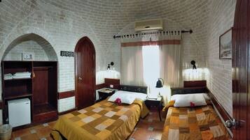 A room with two beds, a wooden wardrobe, a small refrigerator, and a brick wall.