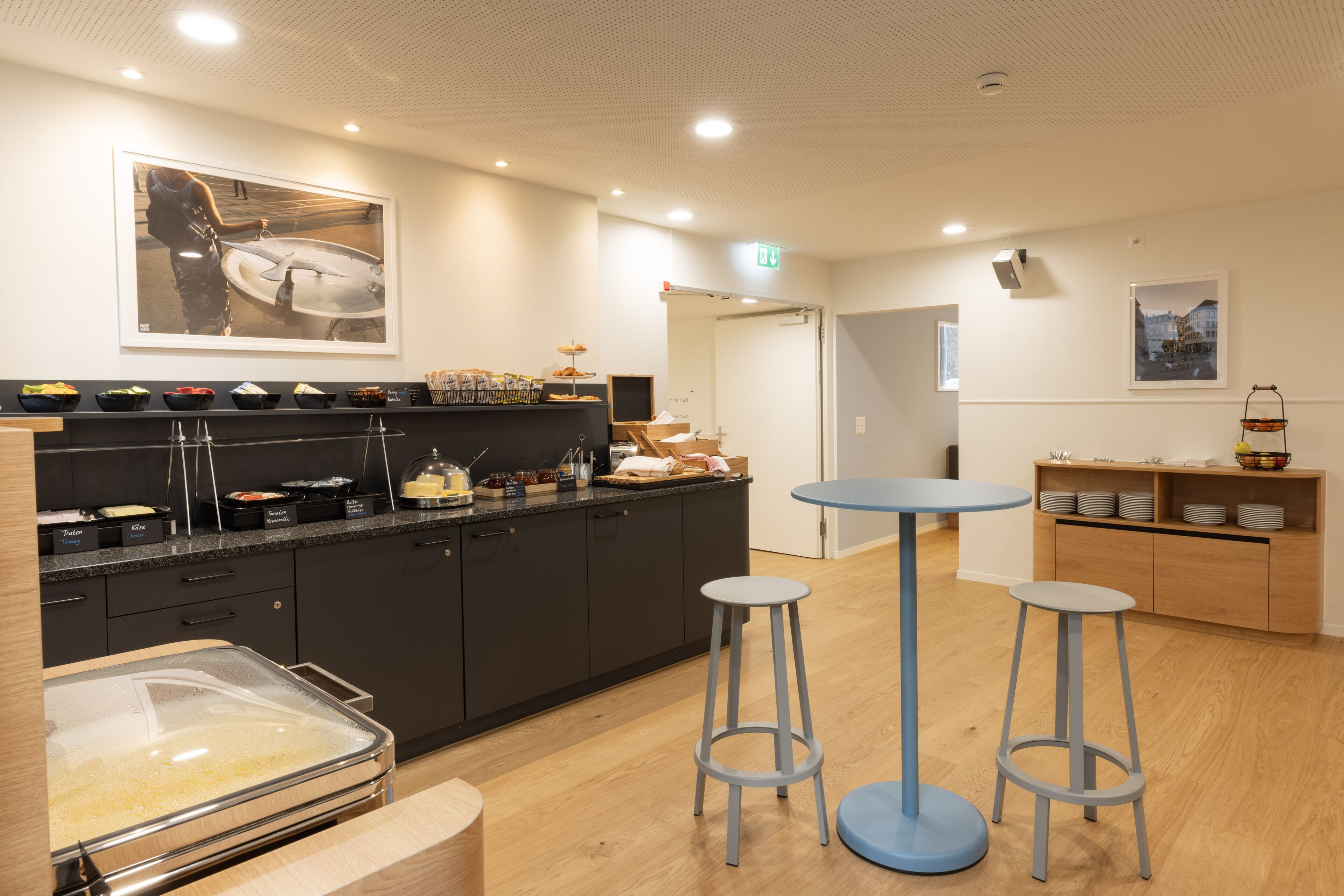 A modern kitchen with a buffet setup, a coffee station, and a seating area with stools.