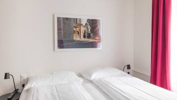 Habitación de hotel con dos camas, un cuadro enmarcado en la pared, una mesita de noche con lámpara y una cortina roja.