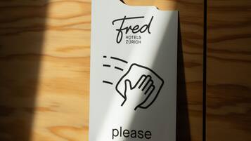 Ein weißes Hotelschild mit Hand-Symbol und dem Text 'fred hotels zurich bitte reinigen'.