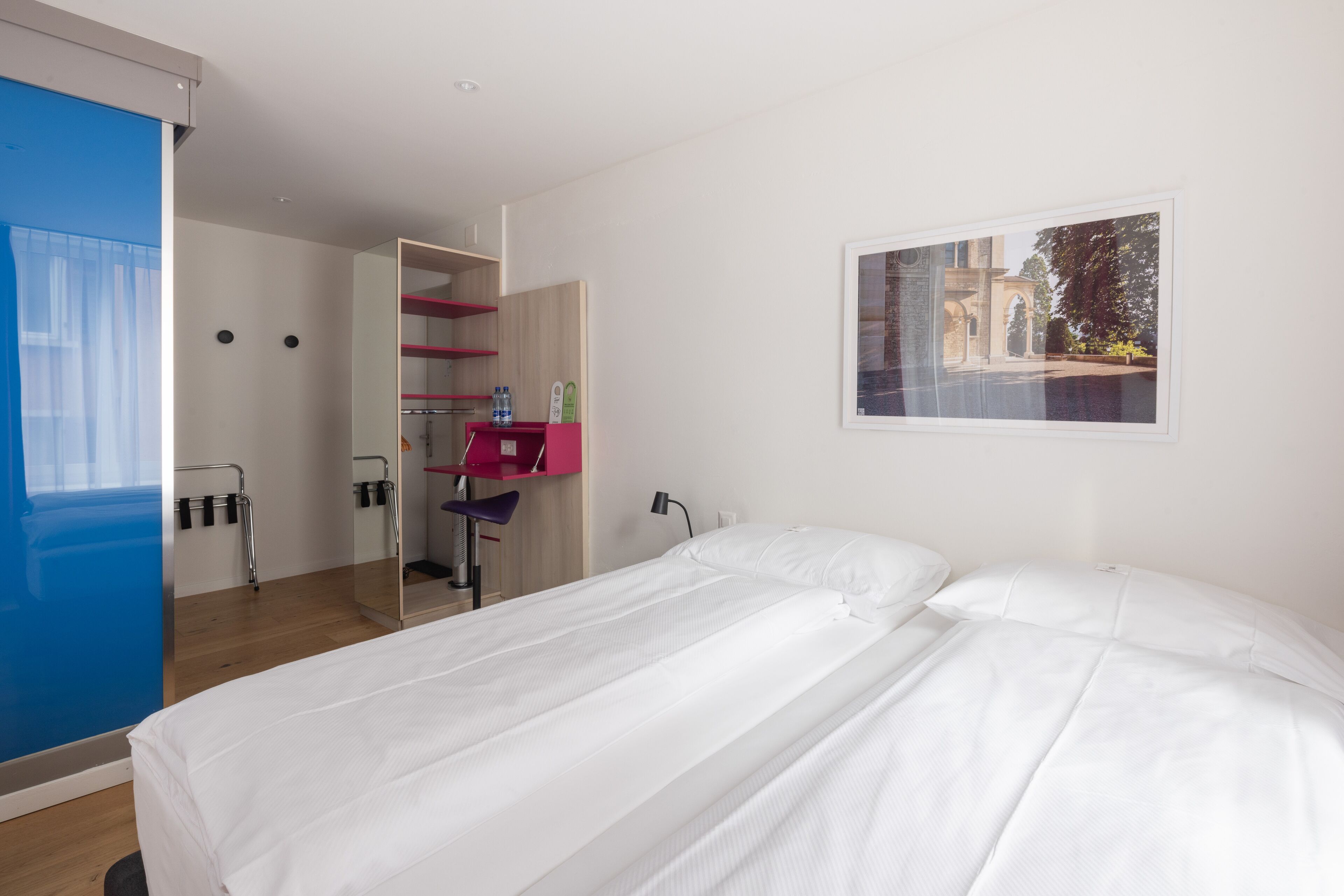 Une chambre d’hôtel moderne avec un grand lit, un miroir, un bureau avec une chaise et un tableau encadré au mur.