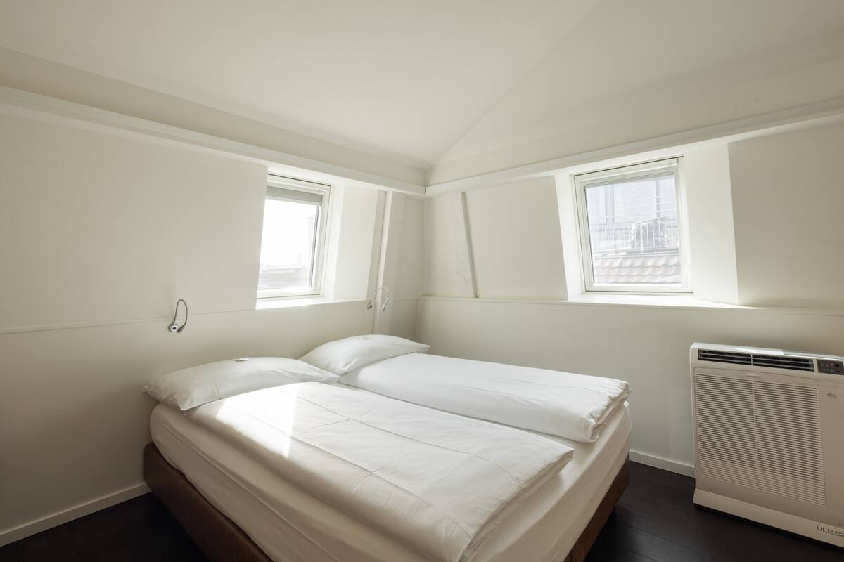 Ein Schlafzimmer mit einem Bett, zwei Fenstern und einer Klimaanlage.