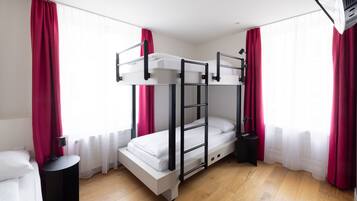 Habitación con literas, una mesita de noche pequeña, una lámpara y una ventana con cortinas.