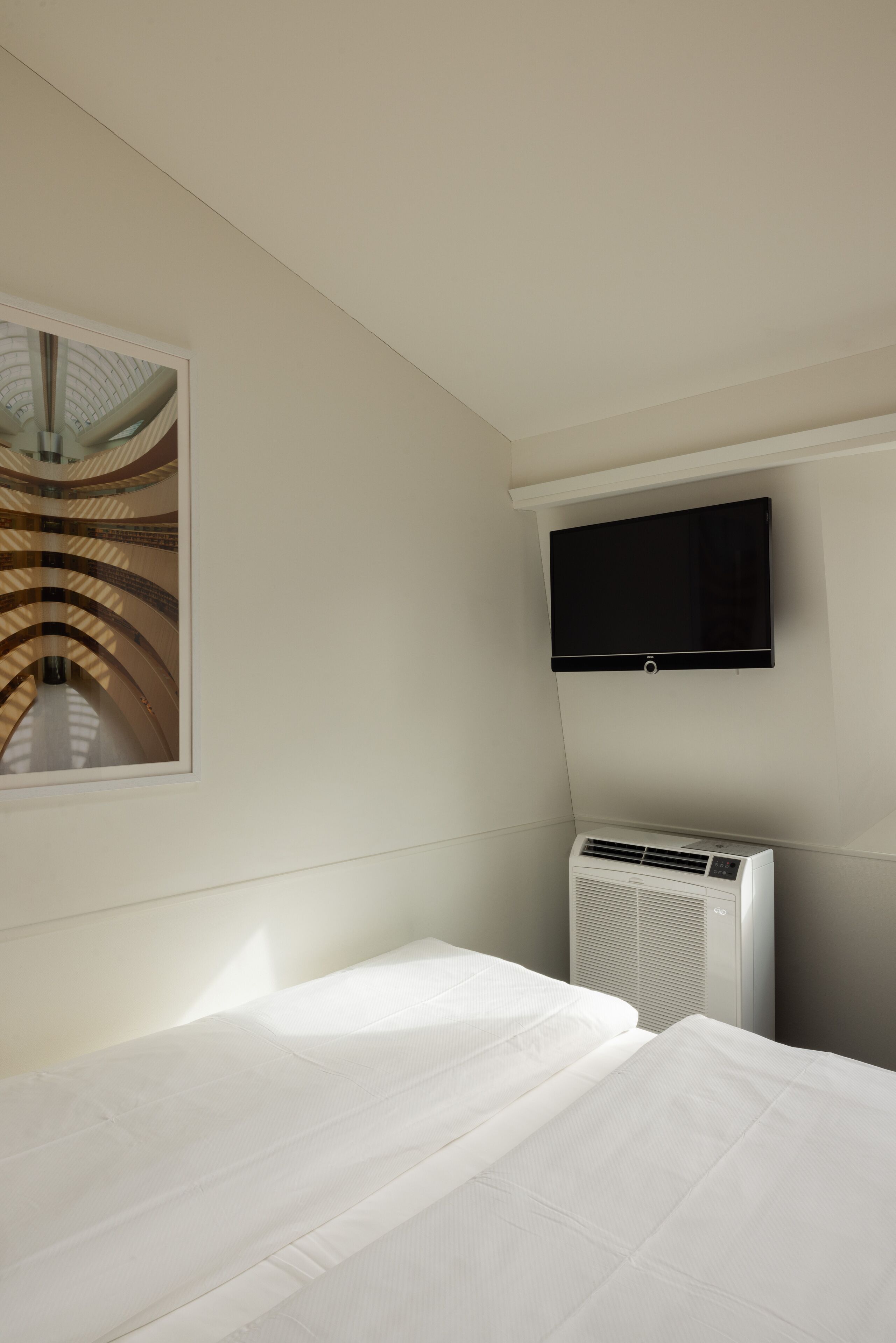 Ein Hotelzimmer mit einem Bett, einem an der Wand befestigten Fernseher und einer Wandklimaanlage.