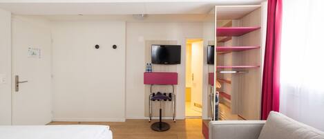 A hotel room with a bed, a sofa, a TV mounted on the wall, and a door leading to a bathroom.