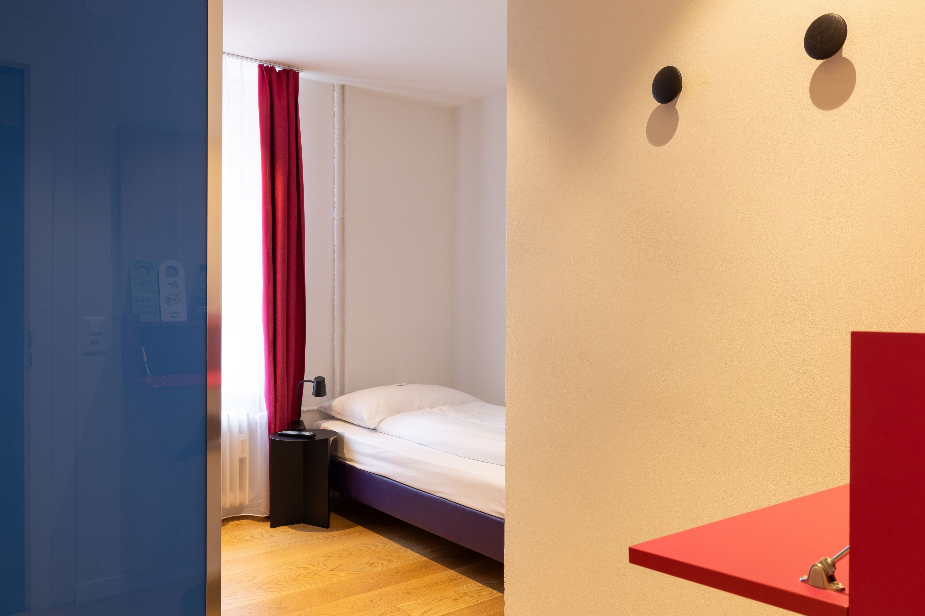 Ein Schlafzimmer mit einem Bett, einem Nachttisch, einem roten Vorhang und Holzboden.
