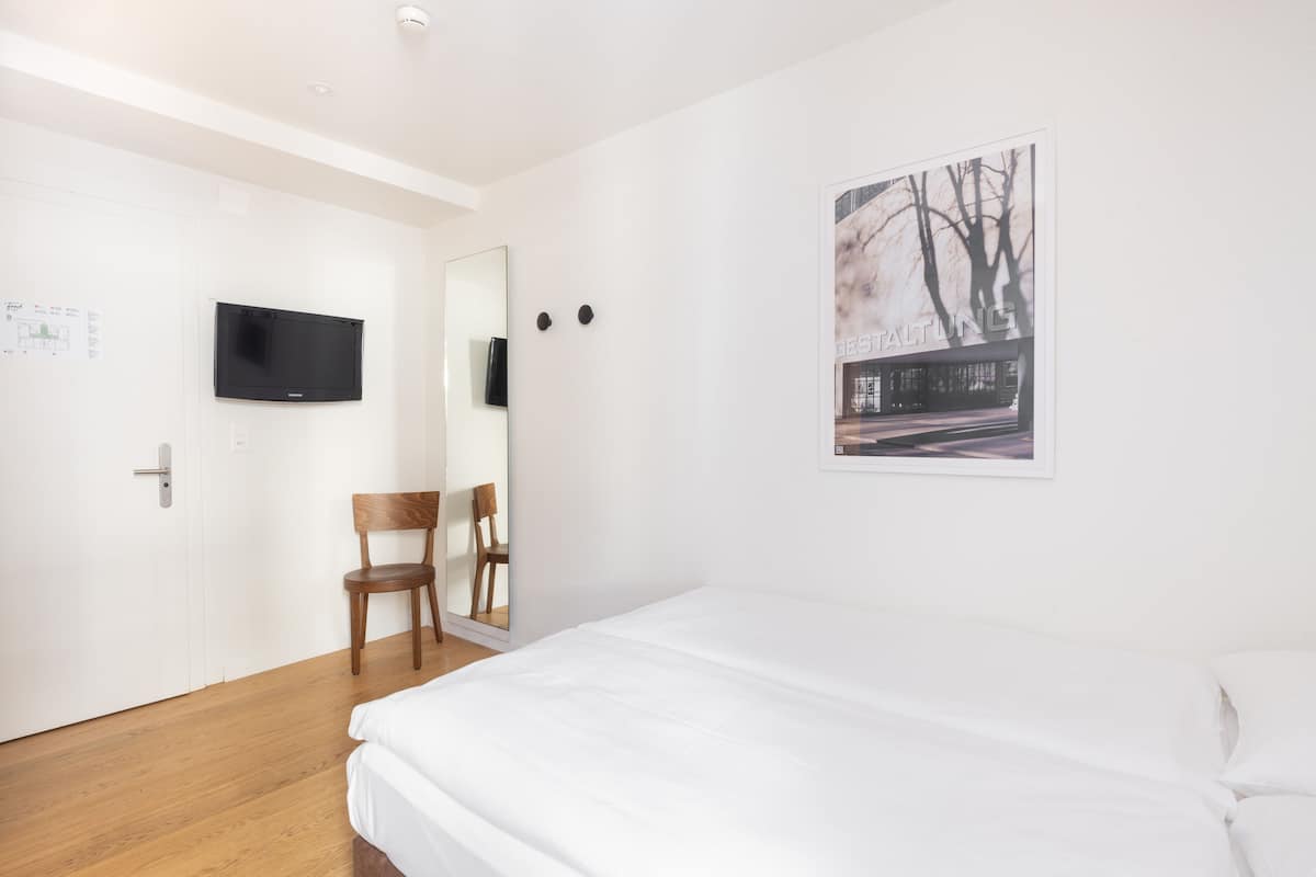 Ein Hotelzimmer mit Bett, Sessel, Wandfernseher und einem Poster an der Wand.