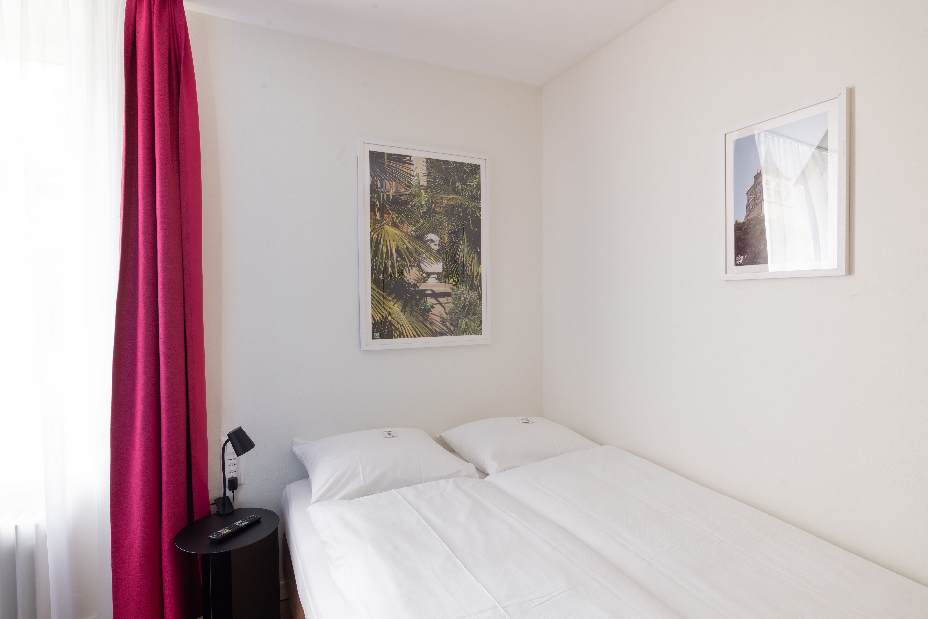 A hotel room with a bed, a nightstand, a lamp, and two framed pictures on the wall.
