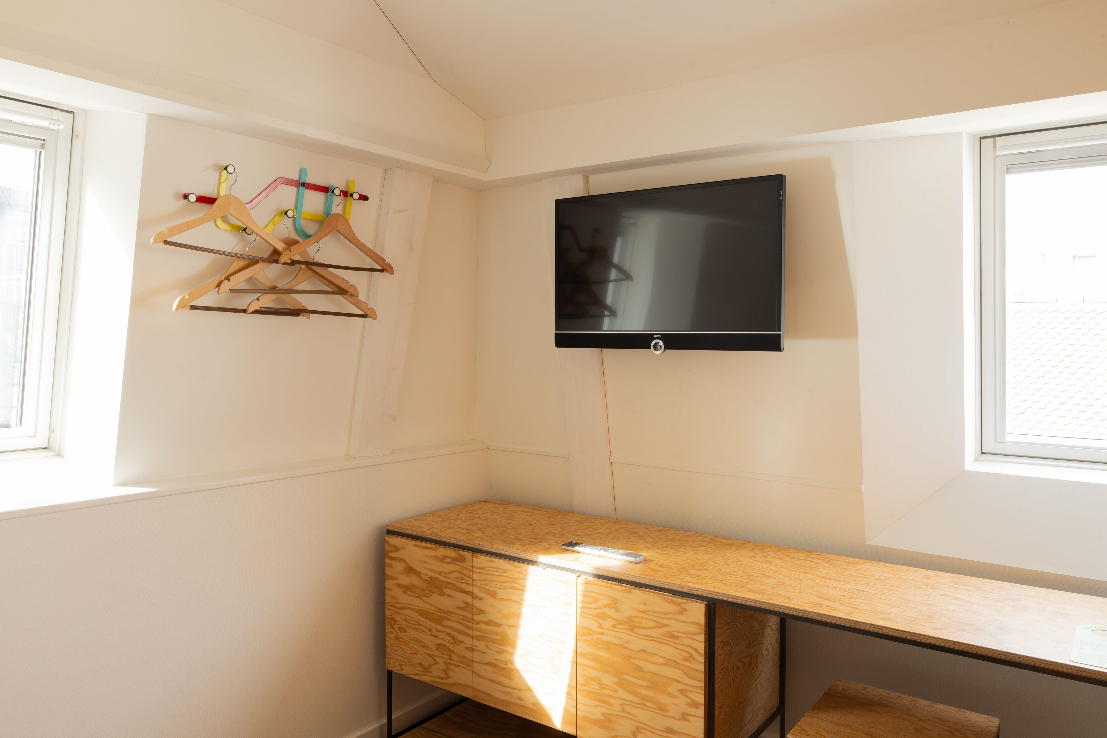 A room with a wooden desk, a TV mounted on the wall, and a window with a view of the outside.