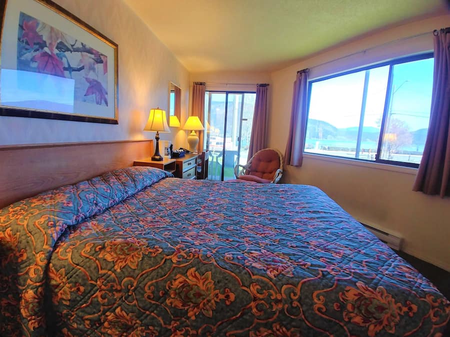 Ein Hotelzimmer mit einem großen Bett, zwei Nachttischlampen, einem Sessel, einem Schreibtisch und einem Fenster mit Vorhängen.